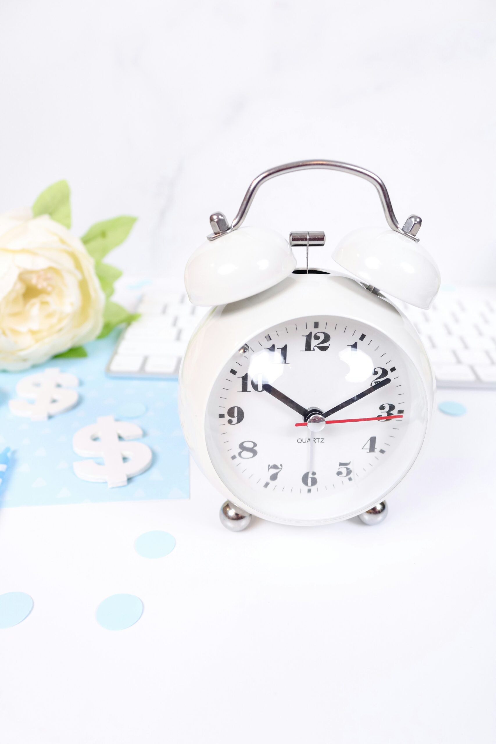 decorative photo of a white alarm clock, some flowers and some decorative dollar signs